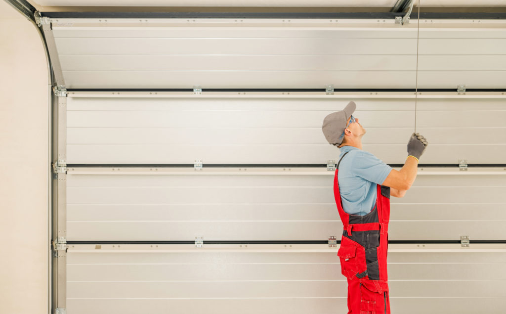 A worker in overalls installing a garage door for a garage door company.