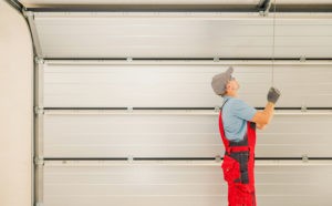 A worker in overalls installing a garage door for a garage door company.